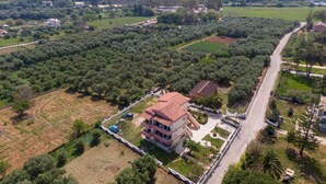 An aerial view of a residential area with a prominent multi-story house featuring a red-tiled roof, surrounded by olive groves and open fields. - Apartment 'Lotus 1' with Sea View, Wi-Fi and Air Conditioning (Corfu)