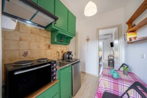 A compact kitchen with a microwave, stove, and sink, green cabinets, and a dining area with a table and chairs. - Apartment 'Lotus 1' with Sea View, Wi-Fi and Air Conditioning (Corfu)