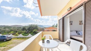Un balcon avec une table et des chaises, une voiture garée devant, et une vue sur la campagne.