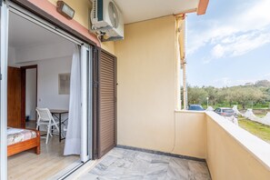 A balcony with a sliding door, a ceiling fan, a view of parked cars, and a table with chairs. - Apartment 'Lotus 3' with Sea View, Wi-Fi and Air Conditioning (Corfu)