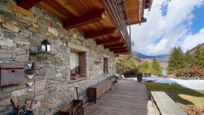 Un edificio de piedra con vigas de madera, una terraza de madera y vistas a montañas.