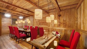 Interior de madera con una mesa de comedor, sillas rojas, luces colgantes y techo de madera.