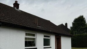 Une maison de plain-pied à l’extérieur blanc, avec des fondations en briques et un toit recouvert de tuiles.