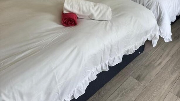 Deux lits simples avec du linge de lit blanc et des têtes de lit sombres, dans une pièce dont le sol est recouvert de parquet.