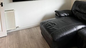 Un salon avec un téléviseur fixé au mur, un radiateur et un canapé en cuir.