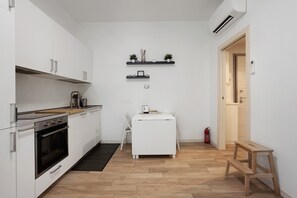 Eine kompakte Küche mit weißen Schränken, einem eingebauten Backofen, einem kleinen weißen Tisch und zwei Wandregalen mit Dekoration.