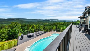 Une terrasse en bois avec une piscine, des chaises longues et une vue sur des collines verdoyantes.
