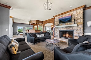 A modern living room with a stone fireplace, black sofas, and a large TV mounted on the wall.