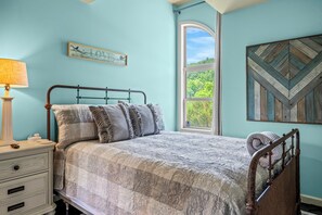 A bedroom with a bed, a nightstand, a lamp, a window with a view of trees, and a wall decoration.