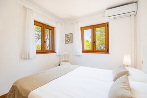 A bedroom with a bed, a chair, a window, and an air conditioning unit.