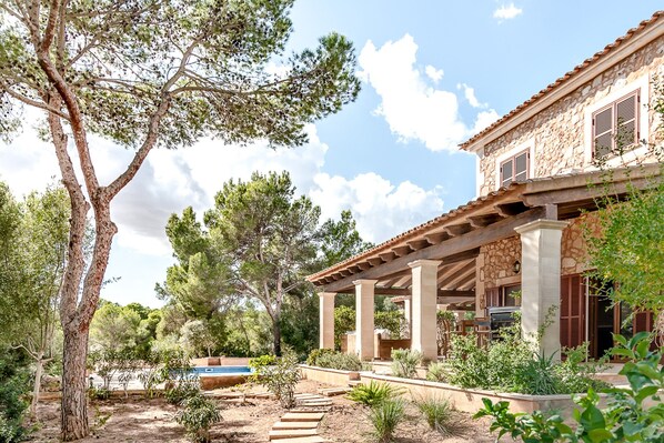 Un edificio de piedra con un patio cubierto, mobiliario exterior y una piscina.