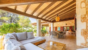 Une terrasse extérieure dotée d’un plafond en bois, d’un canapé, d’une table et d’un mur en pierre.