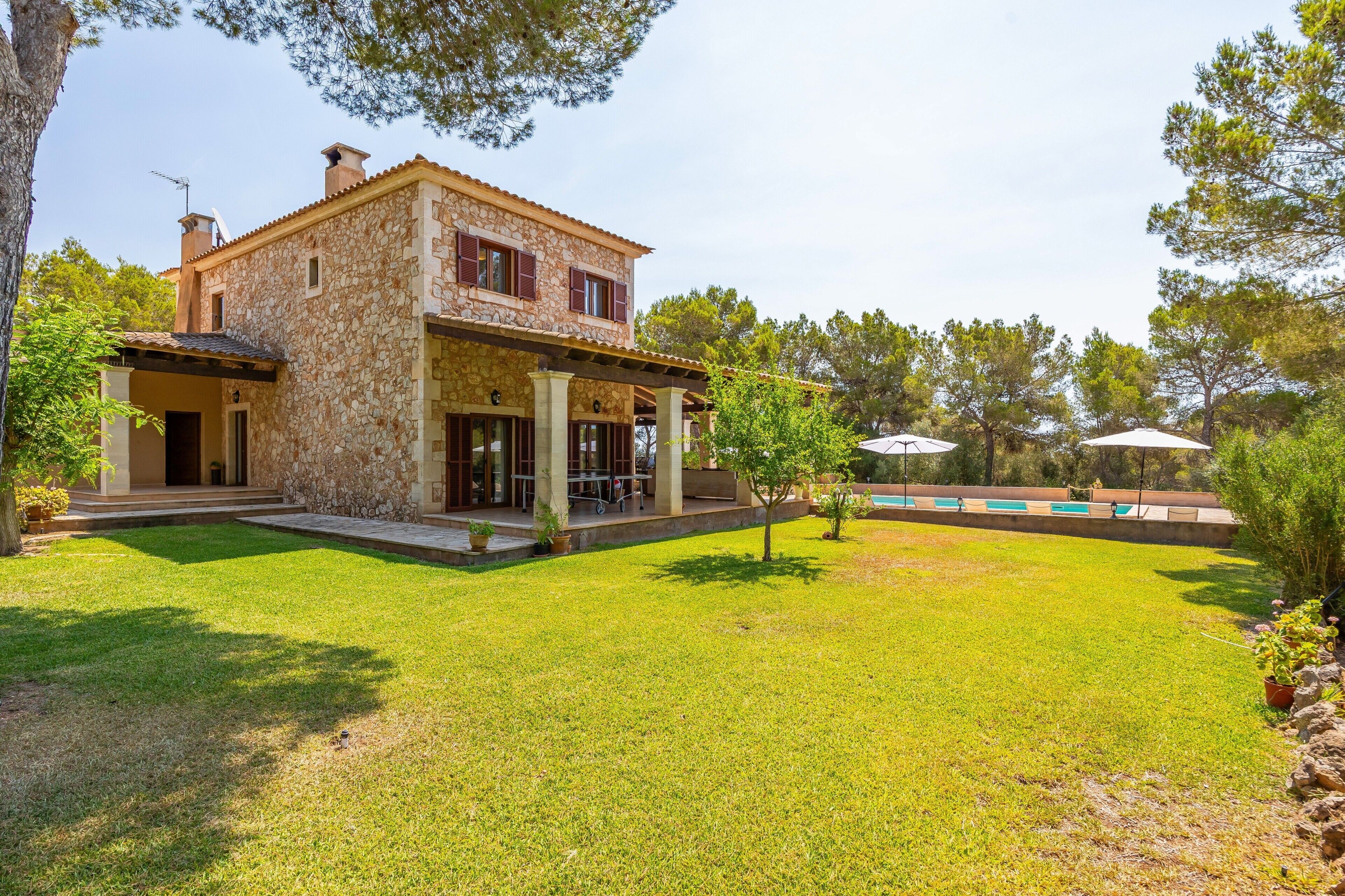 Une maison en pierre avec une piscine, entourée d’une pelouse bien entretenue et d’arbres.