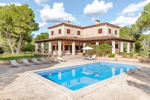 Una casa de piedra de dos pisos con piscina, mobiliario de exterior y un jardín.