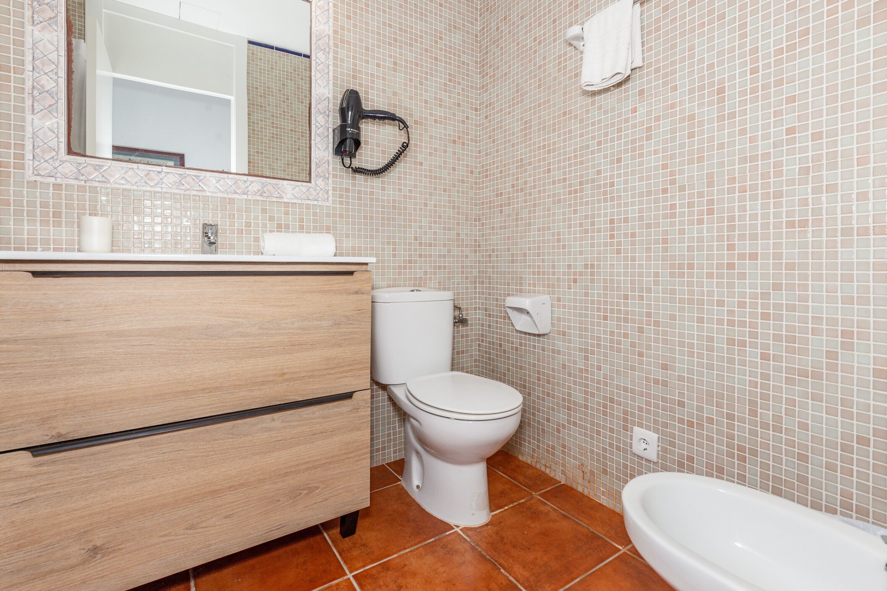 Un baño con tocador de madera, inodoro y lavamanos blancos.