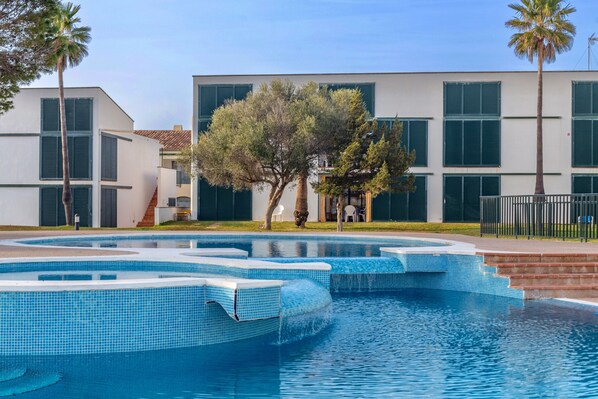 Una piscina con diseño geométrico, rodeada por un edificio con ventanas amplias y un árbol.