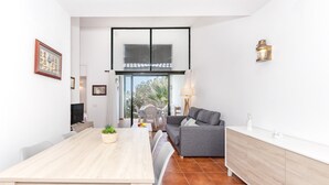 Un espacio habitable moderno con comedor, sofá, televisor y vista a través de una puerta de cristal.