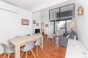A modern living room with a sofa, a dining table with chairs, a TV, and a large window.