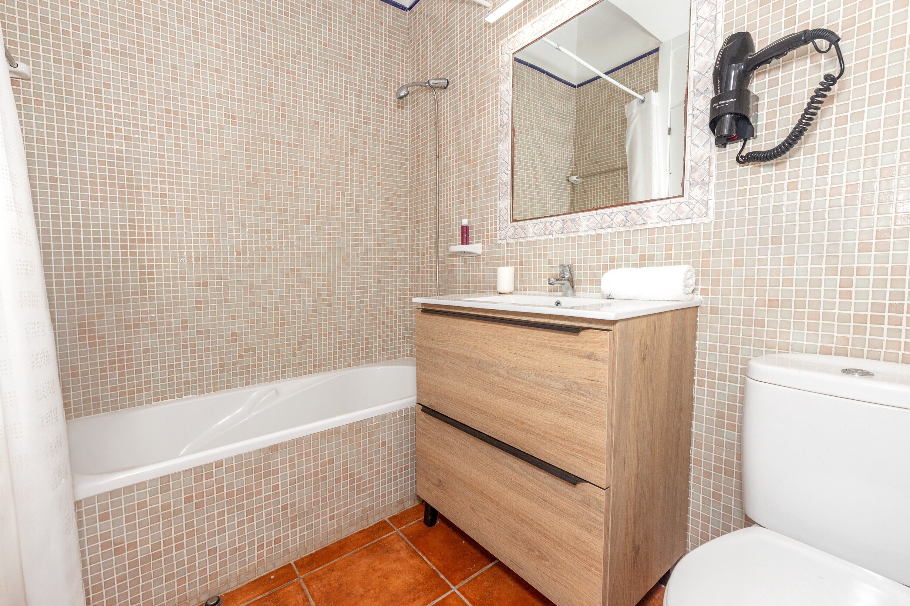 A bathroom with a bathtub, a wooden vanity with a mirror, and a toilet.