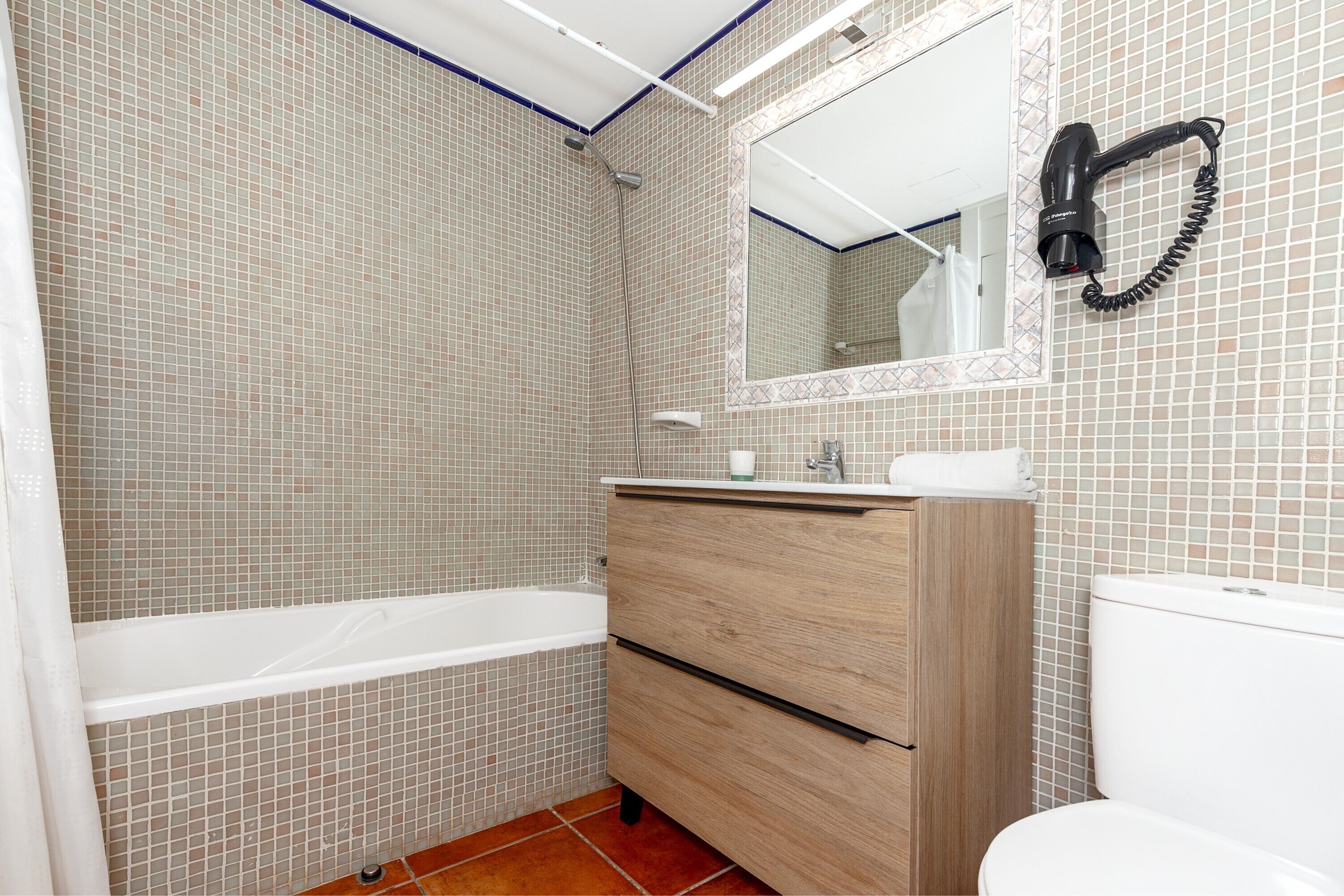 A bathroom with a bathtub, a wooden vanity, a mirror, and a hairdryer mounted on the wall.