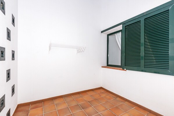 A room with a tiled floor, a window with green shutters, and a wall-mounted air conditioning unit.