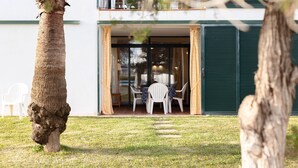 A modern building with a glass door entrance, a patio with a table and chairs, and a lawn.