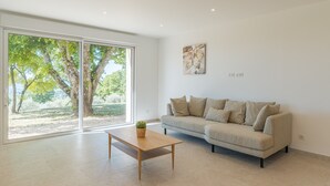 Una sala de estar moderna con un sofá, una mesa de centro y un amplio ventanal corredero que da a un espacio exterior.