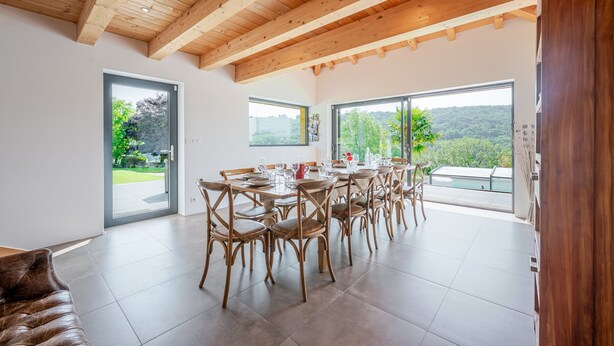A spacious dining area with wooden beams, large windows, and a view of greenery.
