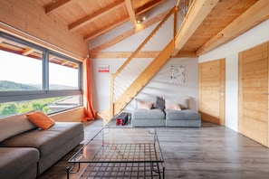 Un intérieur moderne avec un escalier en bois, un canapé, une table basse en verre et une vue dégagée grâce à de grandes fenêtres.