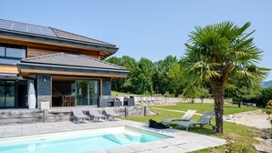 A modern house with a swimming pool, outdoor seating, and a palm tree.