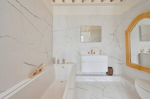 Une salle de bain avec une baignoire, un lavabo, un miroir et des murs en marbre.