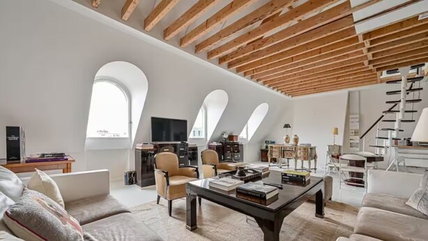 A spacious loft with high ceilings, exposed wooden beams, and large arched windows.