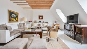 A modern loft with a high ceiling, exposed wooden beams, a living area with sofas, a coffee table, and a TV on a wooden cabinet.