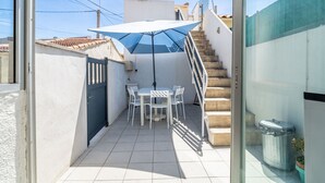 Un petit pati amb taula i cadires, una ombrell blanca i una escala.