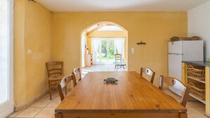 Un comedor con mesa de madera, sillas, un refrigerador y vistas a un patio a través de un arco.