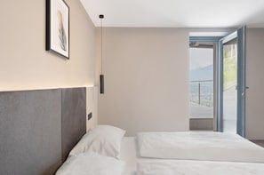 Un dormitorio moderno con cama, una obra de arte enmarco, una lámpara colgante y vistas a través de un ventanal.