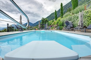 Ein Pool mit Liegestühlen und Sonnenschirmen, umgeben von viel Grün und Bergen.