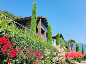 A building with a wooden facade, surrounded by lush greenery and flowering plants.
