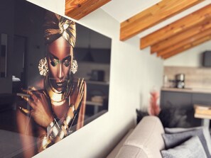 Un interior moderno con una gran obra de arte enmarcada, vigas de madera y una cocina al fondo.
