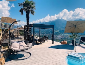 Een dakterras met een zwembad, een hangstoel, ligbedden, een pergola en uitzicht op het landschap.