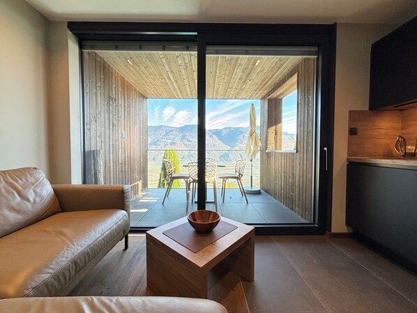 A modern living room with a sofa, a wooden coffee table, and a view of mountains through a sliding door. - Apartment 'Victoria' with Mountain View, Shared Pool and Wi-Fi (Marling)