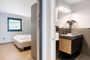 A modern bedroom with a bed, a bathroom with a sink and mirror, and a window with a view. - Apartment 'Victoria' with Mountain View, Shared Pool and Wi-Fi (Marling)