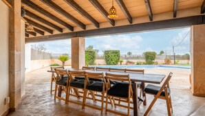 An outdoor covered dining area with wooden tables and chairs, a view of a swimming pool, and a clear sky. - Holiday Home 'Sant Blai Nou' with Private Pool, Private Terrace and Wi-Fi (Illes Balears)