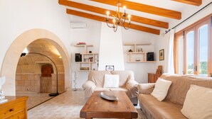 A cozy living room with a fireplace, wooden beams, a sofa, a coffee table, and built-in shelves. - Holiday Home 'Sant Blai Nou' with Private Pool, Private Terrace and Wi-Fi (Illes Balears)