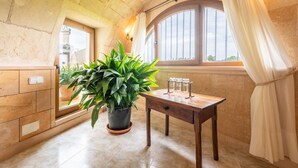 A room with a large potted plant, a wooden table with glasses, a window with curtains, and a stone wall. - Holiday Home 'Sant Blai Nou' with Private Pool, Private Terrace and Wi-Fi (Illes Balears)