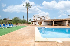 Une piscine avec des chaises longues, un espace patio et un bâtiment doté d’un toit en tuiles.