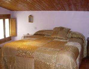 A bedroom with a large bed, wooden ceiling, a small bedside table, and a window. - Country House 'El Rey' with Mountain View, Private Garden and Wi-Fi (Murillo De Gállego)
