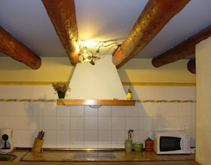 A kitchen with wooden beams, a white tiled backsplash, a wooden shelf with flowers, a microwave, and a coffee maker. - Country House 'El Rey' with Mountain View, Private Garden and Wi-Fi (Murillo De Gállego)