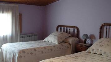 Un dormitorio con dos camas individuales, una mesita de noche con lámpara, un radiador y una ventana con cortinas.