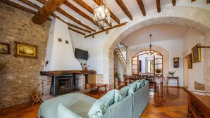 Uma sala de estar rústica com vigas de madeira aparentes, lareira, sofá e um espaço para refeições.